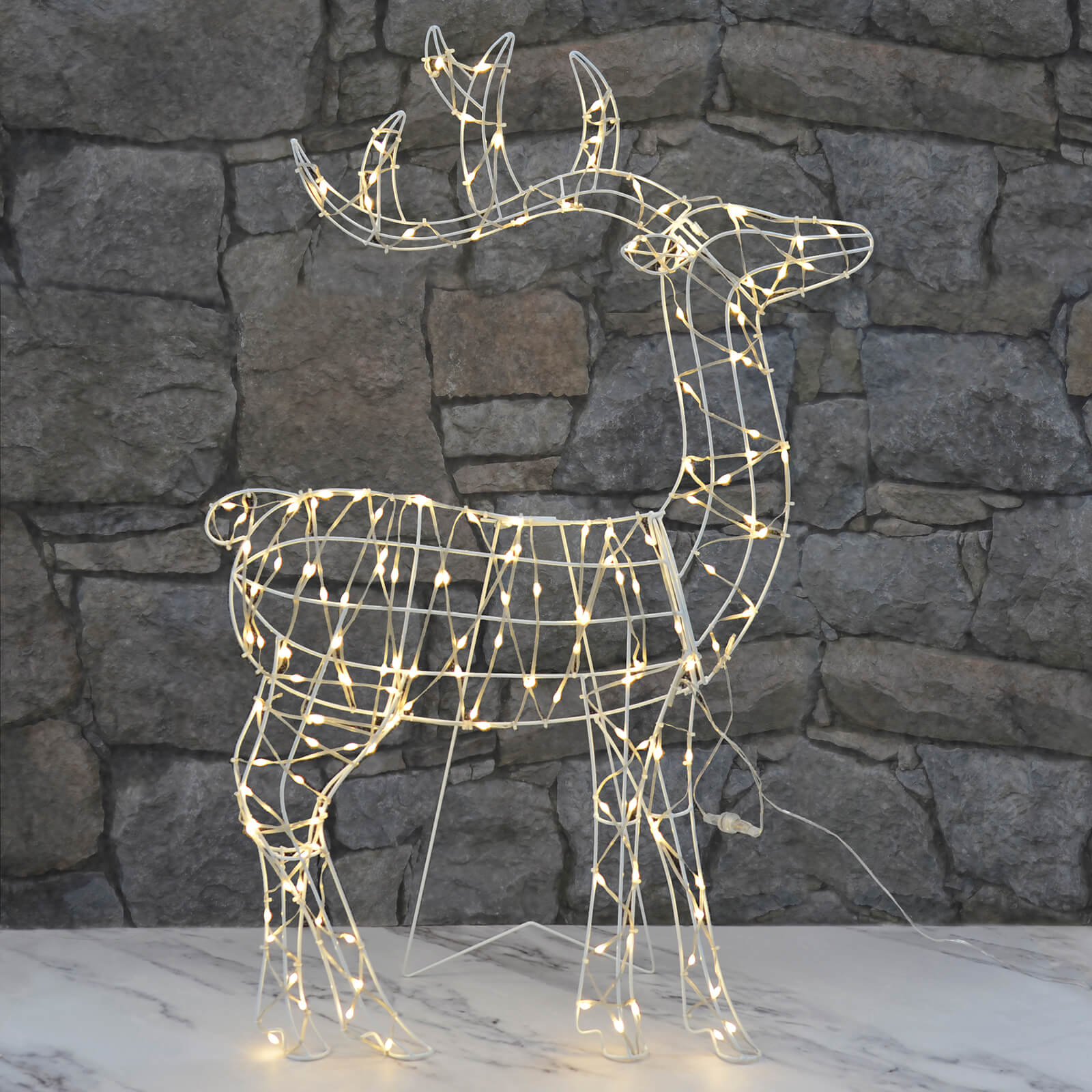 Light up reindeer silhouette Christmas decoration lit by warm white LED lights standing on a patio with brick wall background